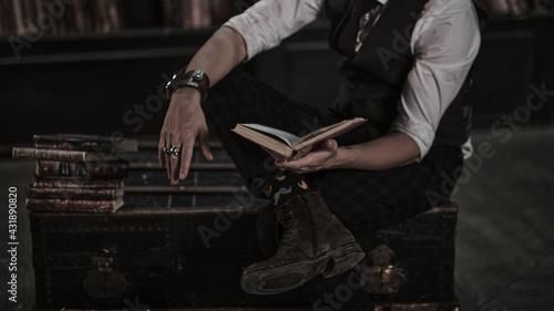 pensive man stands at night in a dark library room and holding a vintage book. stylish man with a mustache straightens the bracelet.