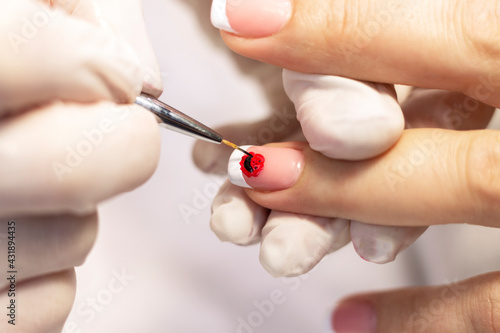 Manicure. Covering natural nails with gel polish  white french coat and nail design in a beauty salon by a manicure master. Close-up