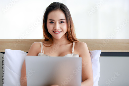 Young Asian female with laptop resting on bed