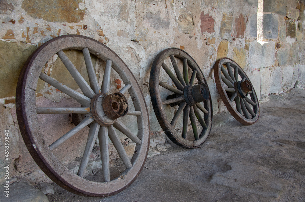 Three old wooden wagon wheels stand in front of a sandstone wall