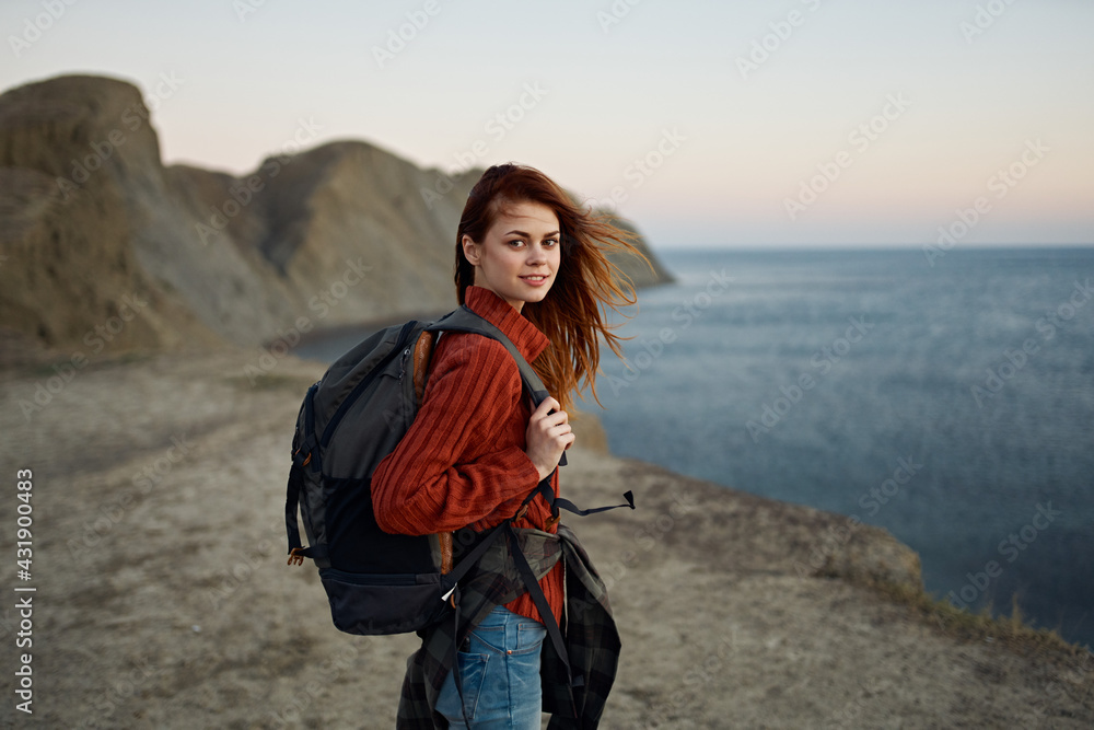 red-haired traveler with a backpack resting on the beach near the sea in the mountains autumn