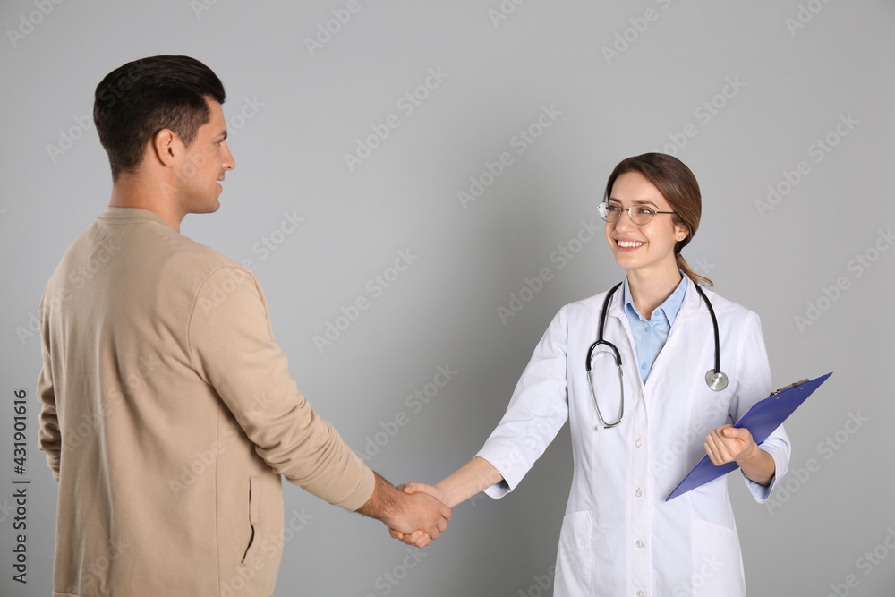 Doctor and patient shaking hands on light grey background Doctor and patient shaking hands on light grey background