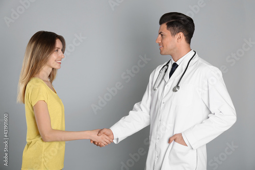 Doctor and patient shaking hands on light grey background