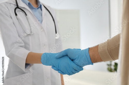 Doctor and patient in protective gloves shaking hands indoors, closeup © New Africa