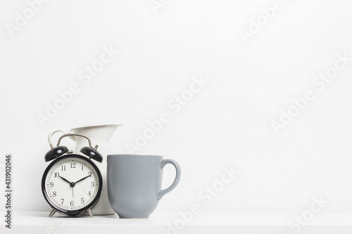 An alarm clock and cup of coffee with white jar on table.