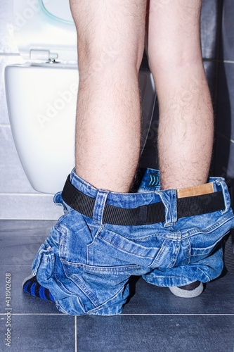 Canvas Print A man is standing by a toilet bowl, having difficulty urinating.