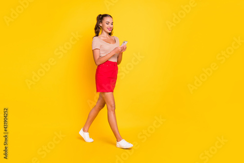Full length body size view of attractive cheerful thin focused girl using device going isolated over bright yellow color background