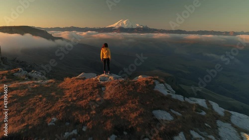 Flight  emotional film tourist people stands on edge of cliff sees snow-capped Elbrus mountain peaks. Mystical fog clouds below. Early morning picturesque epic natural landscape Russia best. 4k