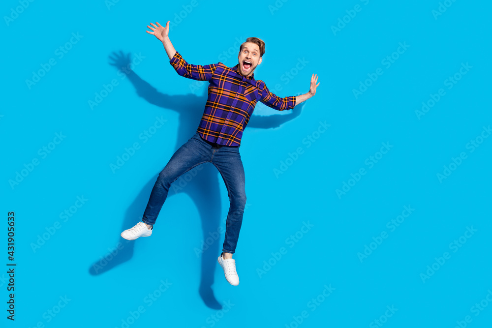 Photo of pretty funny young guy wear plaid clothes flying jumping smiling isolated blue color background