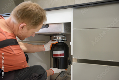 The worker is installing a household waste shredder for the kitchen sink.