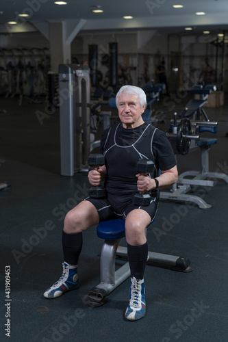 an elderly man working out in the gym stands with a barbell on his shoulders
