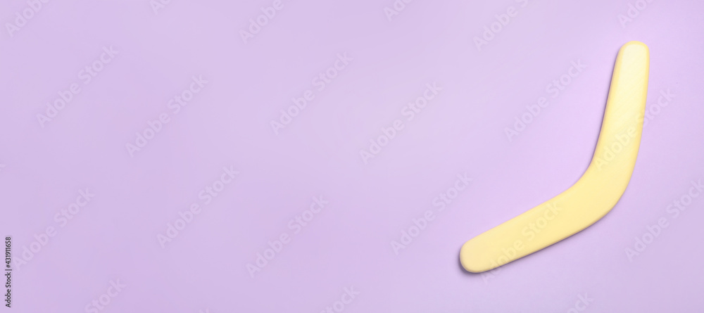 Yellow wooden boomerang on lilac background, top view. Space for text Yellow wooden boomerang on lilac background, top view. Space for text
