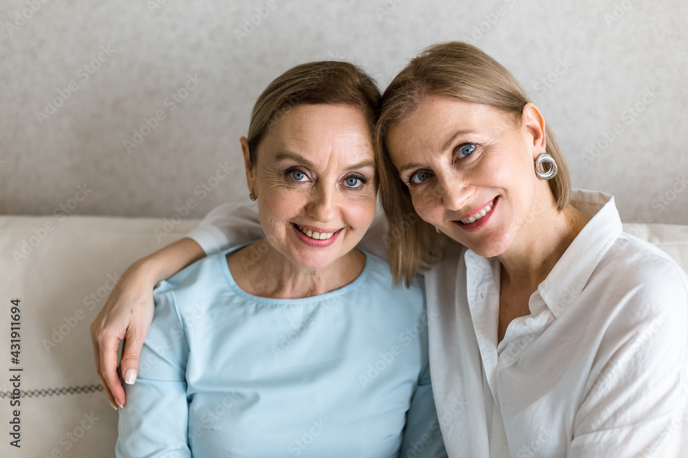 Two adult women are sitting on the couch embracing and looking at the camera. Two adult women are sitting on the couch embracing and looking at the camera.