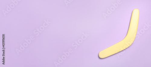 Fototapeta Naklejka Na Ścianę i Meble -  Yellow wooden boomerang on lilac background, top view. Space for text