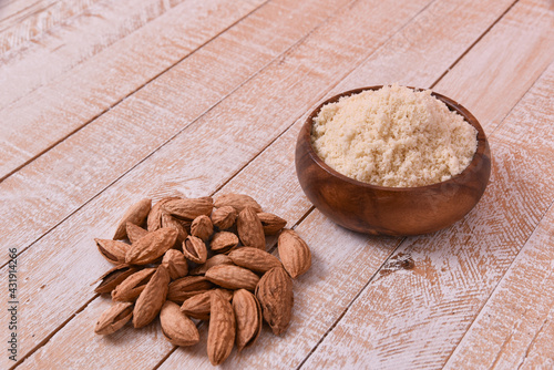 almond flour in a wooden bowl on a white wooden table with a handful of nuts