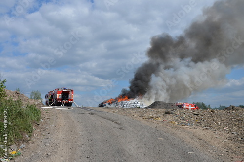 Fire trucks at scene of massive fire in a large landfill with thick black smoke and large flames  © Tom