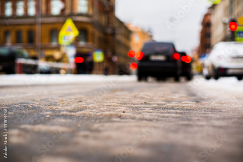 Snowy winter in the big city, the cars stopped at red traffic light signal. Close up view from the asphalt level
