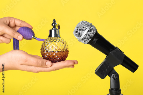 Woman making ASMR sounds with microphone and perfume on yellow background, closeup photo