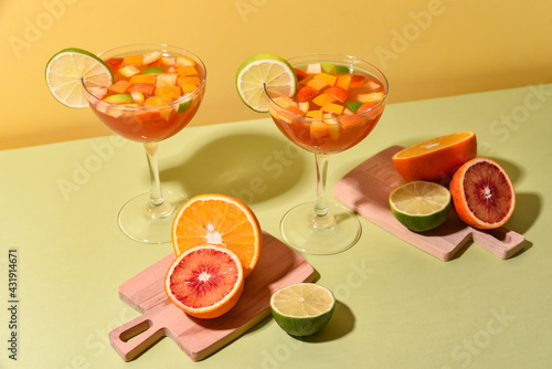 citrus cocktails in glasses on high legs with sliced fruits on a yellow-green background