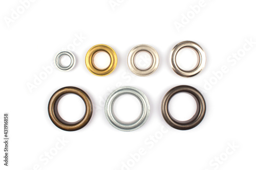 Catalogue photo of different brass multicoloured metal eyelets or rivets - curtains rings for fastening fabric to the cornice, isolated on white background with copyspace for text. Selective focus