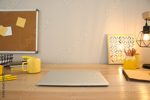 Stylish workplace with laptop on wooden desk near light wall. Interior design