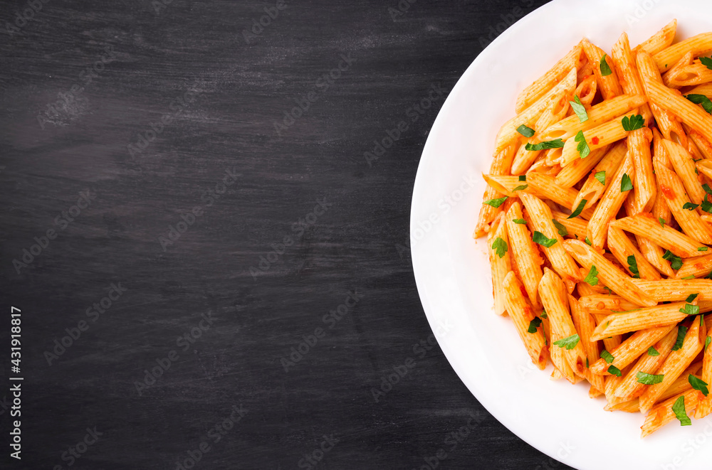Penne pasta in tomato sauce, decorated with parsley on a black background