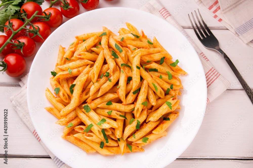 Penne pasta in tomato sauce, decorated with parsley on a white wooden table Penne pasta in tomato sauce, decorated with parsley on a white wooden table