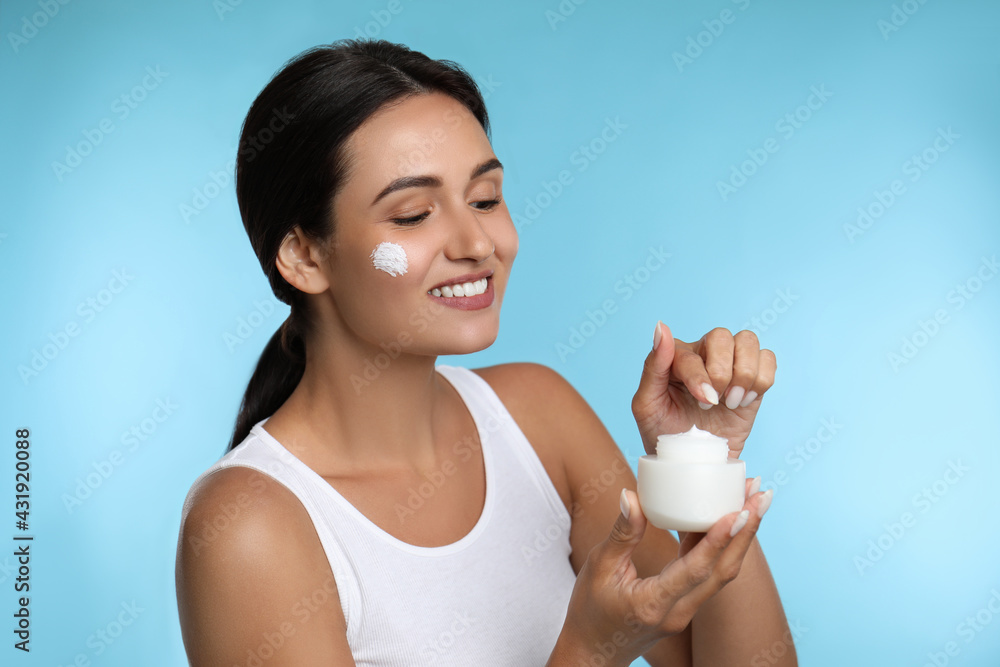 Young woman applying facial cream on light blue background Young woman applying facial cream on light blue background
