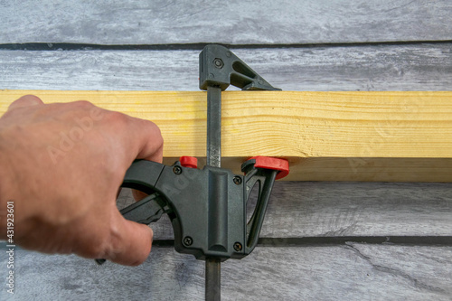A clamp in the carpenter's hand and a wooden bar.