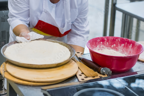 Baker, chef hands preparing fresh dough for ossetian pie on kitchen table at cuisine of restaurant, bakery. Professional cooking, catering, culinary, gastronomy and food concept photo