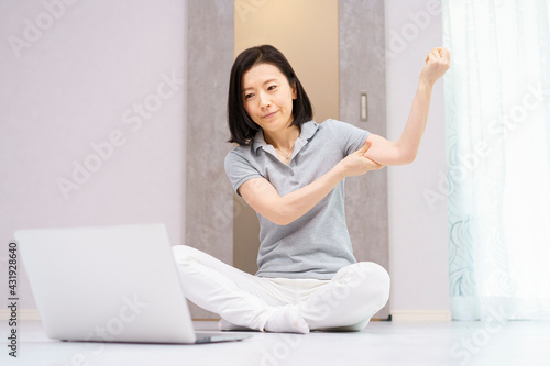 パソコンを見ながら軽い運動をする女性（40代、50代イメージ）