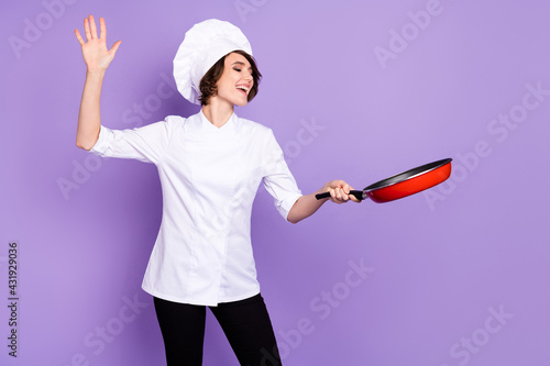 Portrait of attractive cheerful chef holding fry pan good mood professional gourmet isolated over bright violet purple color background