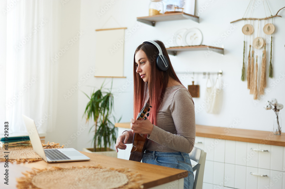 A young teacher teaches remotely using a laptop webcam. A woman teaches to play the ukulele. A young teacher teaches remotely using a laptop webcam. A woman teaches to play the ukulele.