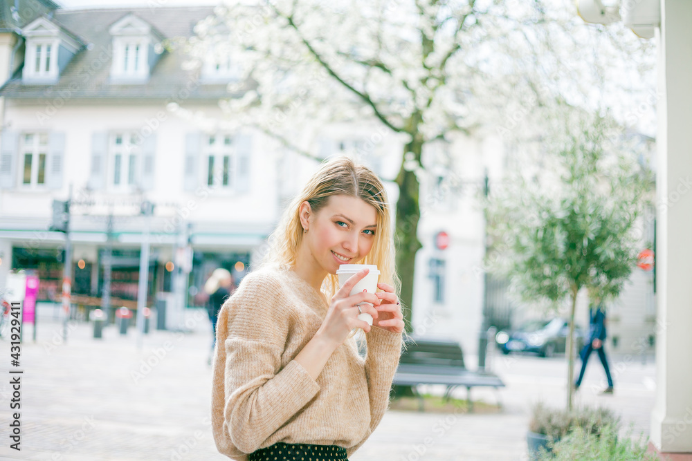 Beautiful young woman drinks coffee to go on the street of a European city. Happiness. Spring.
