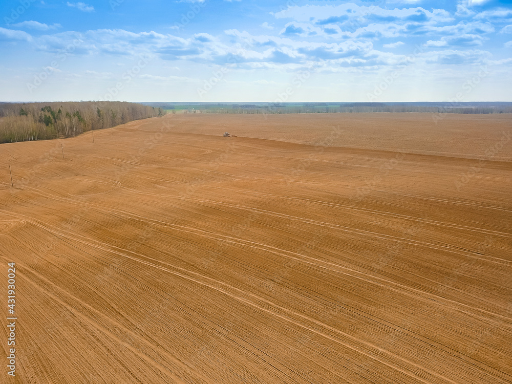 Obraz premium Red tractor plows, cultivates a huge field on a spring day with a blue sky. Photo with a drone