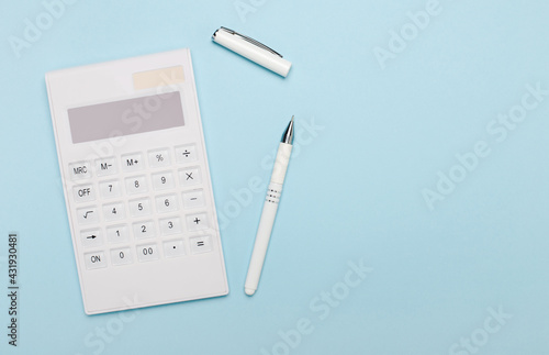 On a light blue background, a white calculator and a white pen. Copy space. Business concept