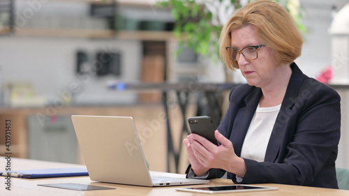 Old Businesswoman Working on Laptop and Smartphone in Office