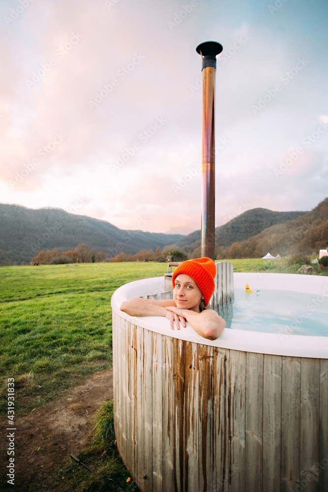 Beautiful young woman lay inside warm hot tub, heated by wood fire. Luxury  outdoor vacation, natural