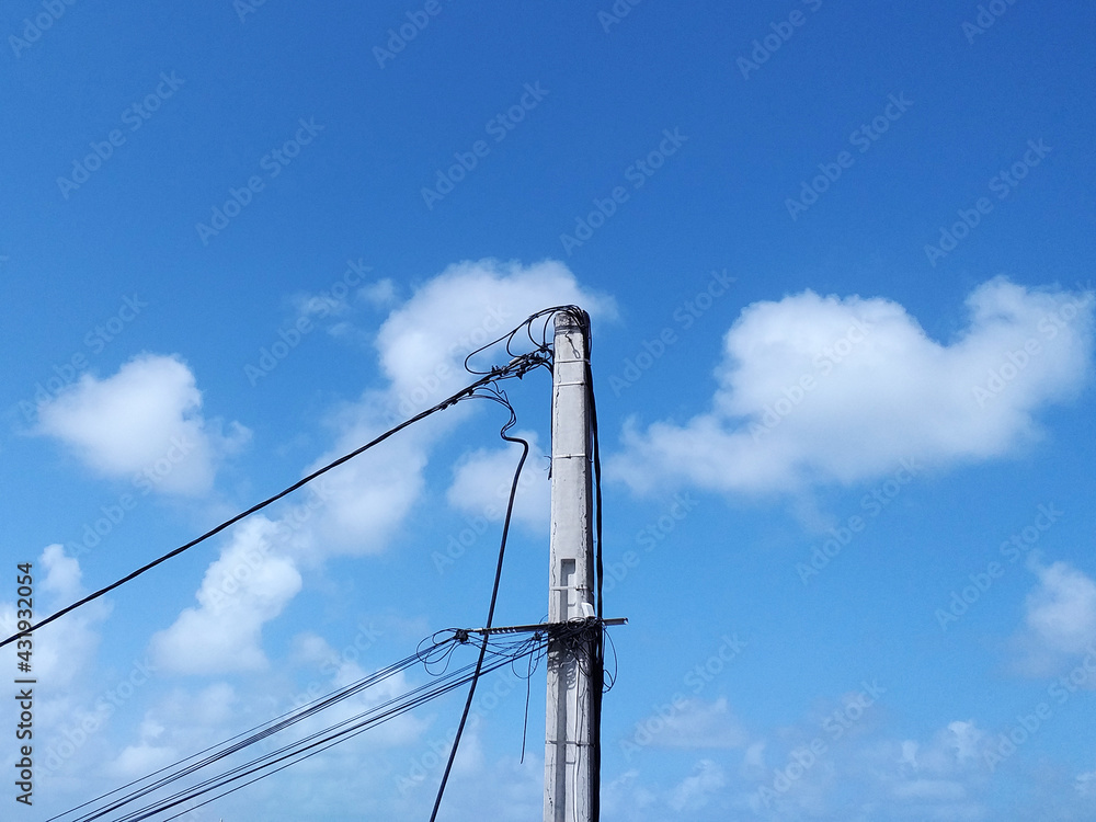 Wooden pole with power lines under tropical blue sky. Bottom view of Wiring on pole, wooden electric pillar. Old electric pole and blue sky. Caribbean Energy and Technology. Wooden pole with power lines under tropical blue sky. Bottom view of Wiring on pole, wooden electric pillar. Old electric pole and blue sky. Caribbean Energy and Technology.