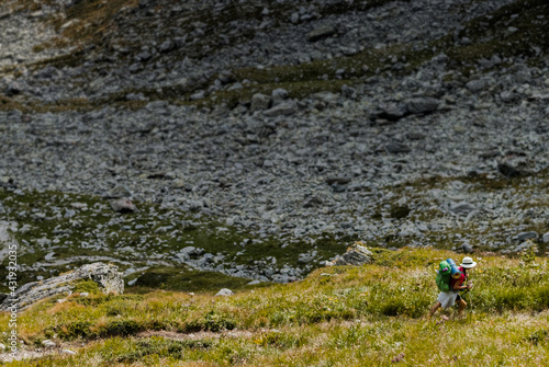Girl traveler with green backpack and hat walking in the mountains.