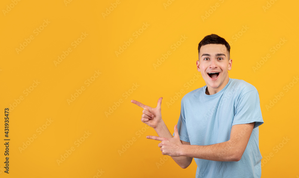 Excited Caucasian guy in casual wear pointing aside at empty space on orange studio background, banner design Excited Caucasian guy in casual wear pointing aside at empty space on orange studio background, banner design