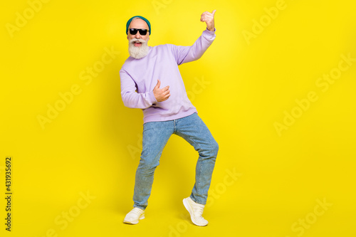 Photo of pretty cute mature man dressed purple pullover headwear spectacles dancing playing guitar isolated yellow color background