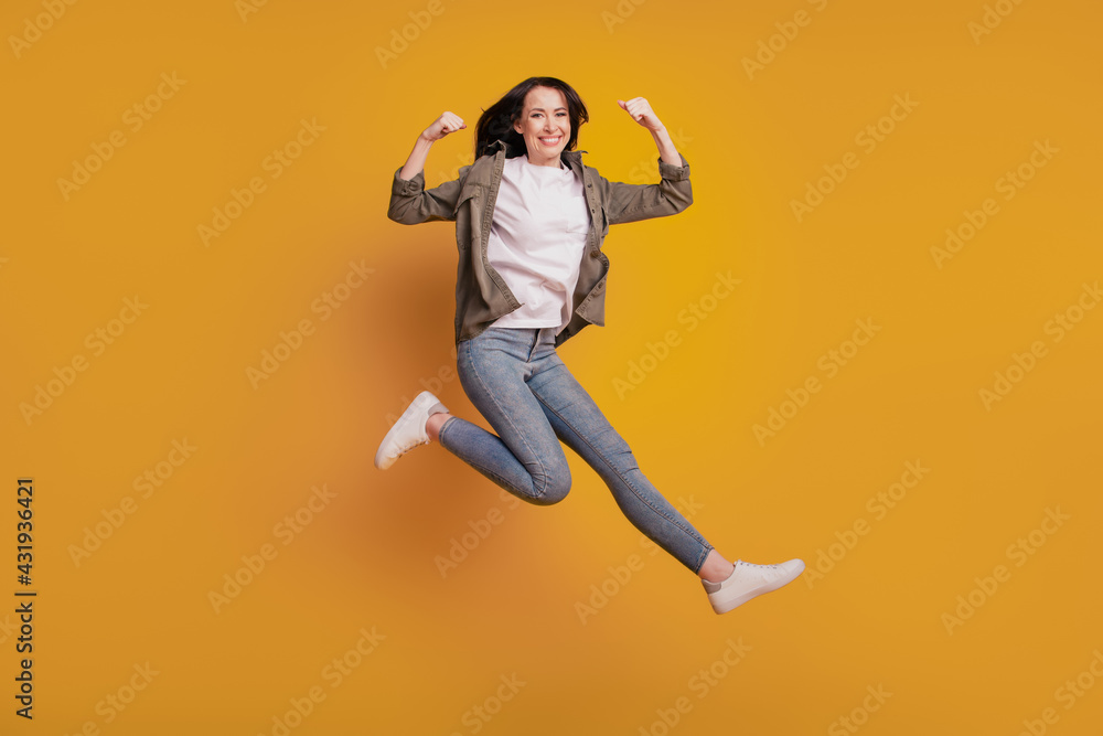 Obraz premium Photo of cheerful lady raise biceps arm jump isolated on yellow background