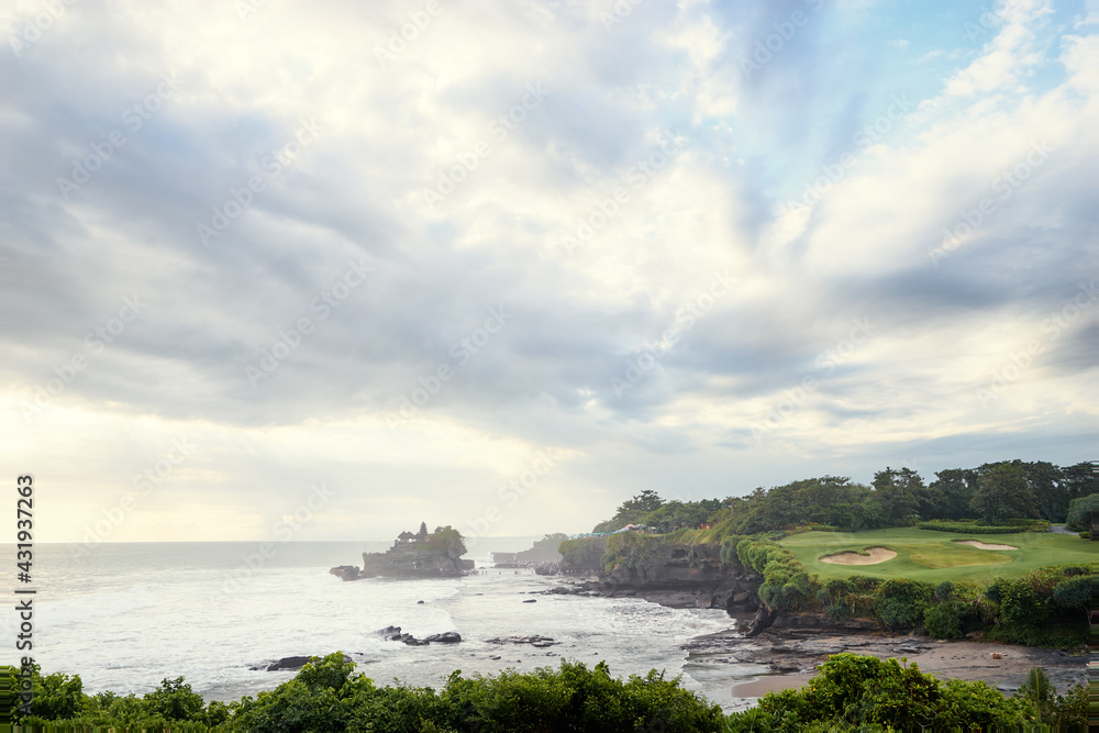 Fototapeta premium Beautiful balinese landscape. Ocean beach. Ancient hinduism temple Tanah lot on the rock against cloudy sky. Bali Island, Indonesia.