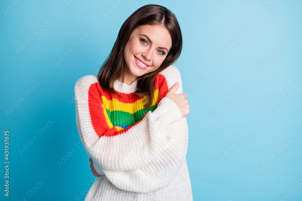 Photo of nice optimistic brunette lady hug herself wear colorful sweater isolated on blue color background Photo of nice optimistic brunette lady hug herself wear colorful sweater isolated on blue color background