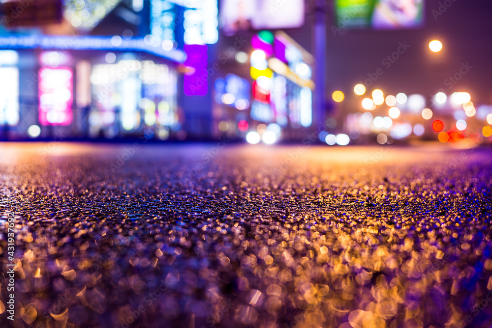 Rainy night in the big city, illumination lights of the shopping center. Close up view from the asphalt level