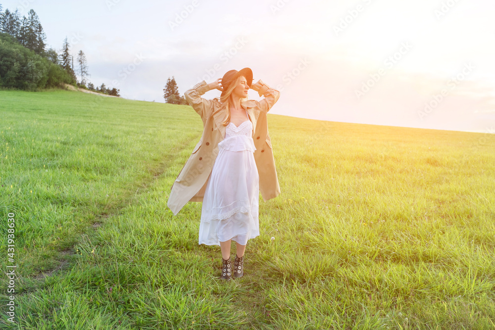 Happy woman enjoying sunset stay on the green grass on the forest peak of mountain. Fresh air, Travel, Summer, Holidays. Health care, authenticity, sense of balance and calmness. Happy woman enjoying sunset stay on the green grass on the forest peak of mountain. Fresh air, Travel, Summer, Holidays. Health care, authenticity, sense of balance and calmness.