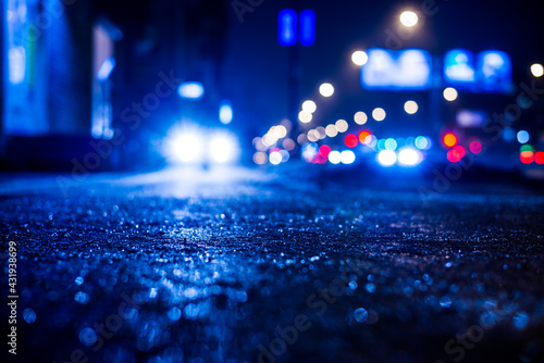 Rainy night in the big city, glare from the headlights of the parked car. Close up view from the sidewalk level © Georgii Shipin