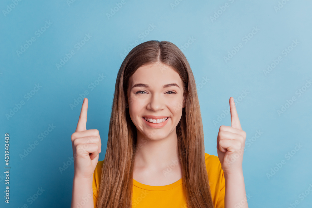 Portrait of positive girl direct forefingers up empty space toothy smile on blue background Portrait of positive girl direct forefingers up empty space toothy smile on blue background