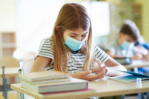 Schoolgirl cleaning hands with disinfecting antibacterial spray